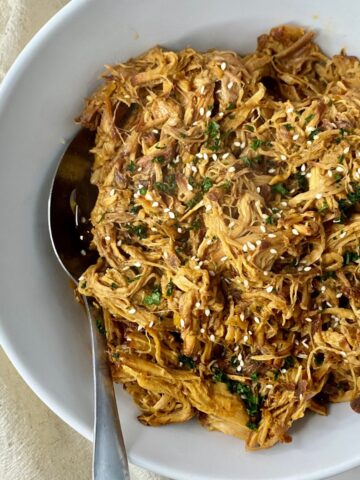A bowl of cooked Slow Cooker Asian Pulled Pork with a spoon.