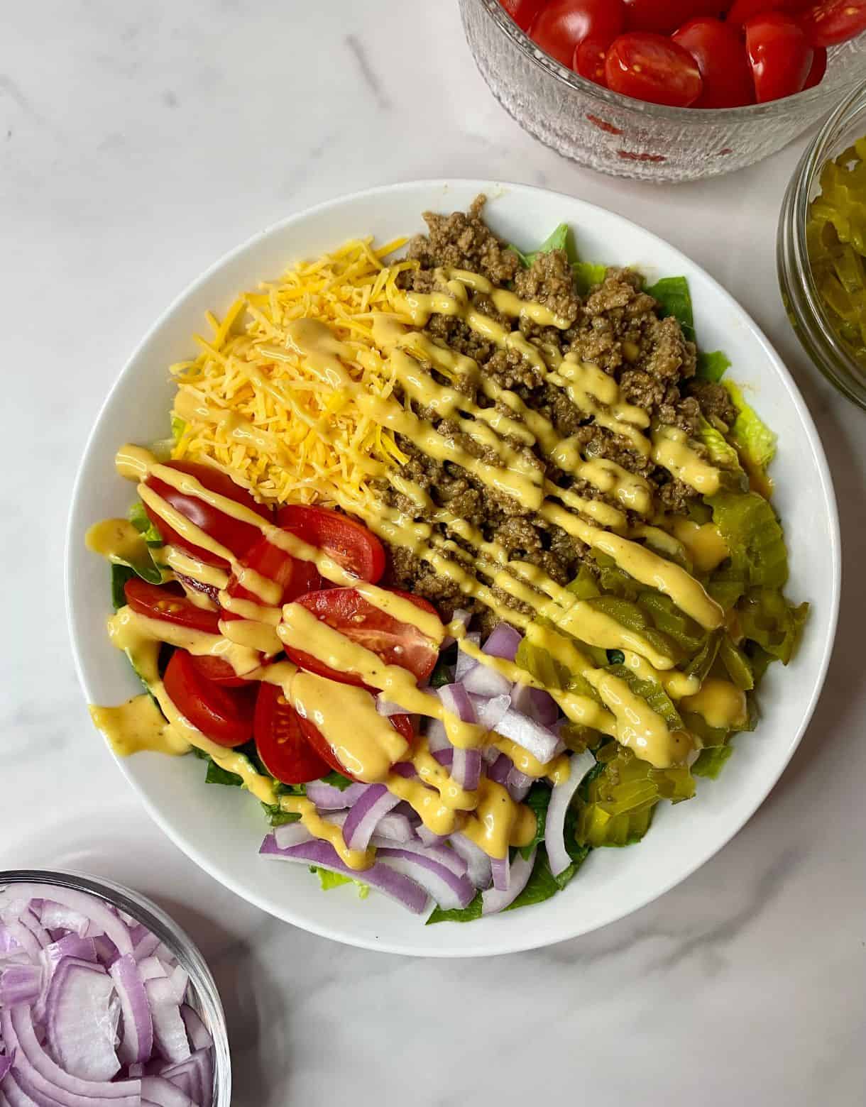 A Burger Bowl with beef, cheese, pickes, lettuce, tomatoes and onions all sprinkled with dressing.