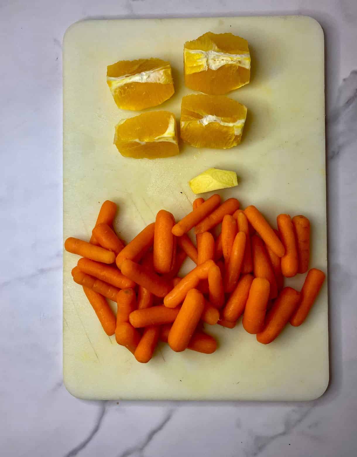 Ingredients prepped for Carrot Orange Ginger Juice. Peeled carrots, peeled chunk of ginger, an orange peeled and quartered.