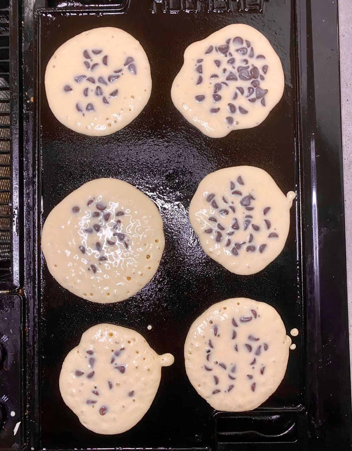 Chocolate Chip Pancakes on a griddle with the tops uncooked.