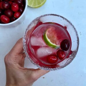 A hand holding a glass of Cranberry Margarita with a salted rim.