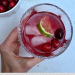A hand holding a glass of Cranberry Margarita with a salted rim.