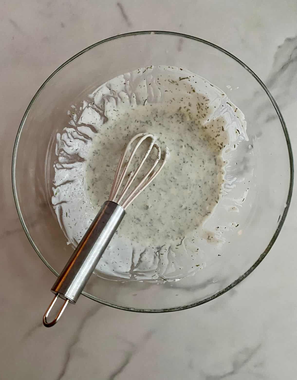 A bowl with a whisk and sour cream dressing in the bowl.