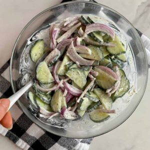 A bowl of Creamy Cucumber and Onion Salad on a checkered kitchen towel.