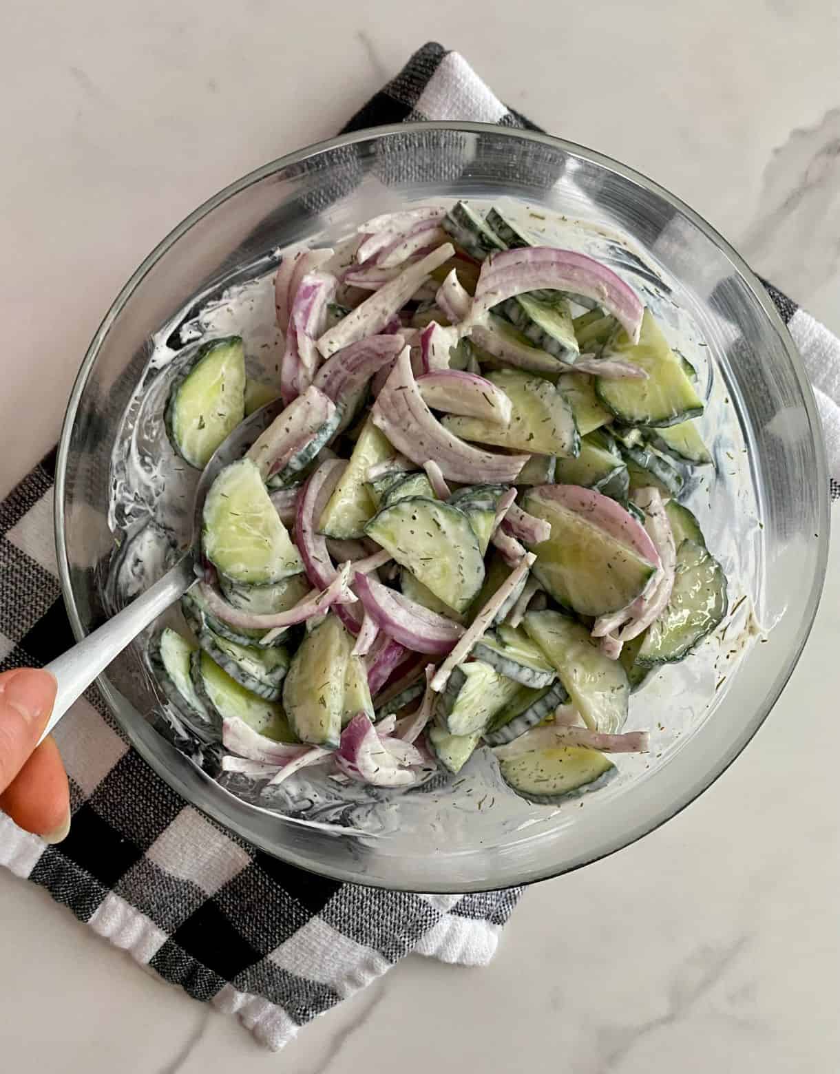 A bowl of Creamy Cucumber and Onion Salad on a checkered kitchen towel.