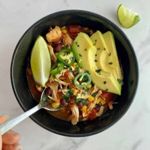 A bowl of Slow Cooker Chicken Tortilla Soup with avocado, a lime wedge and sliced jalapenos on top.