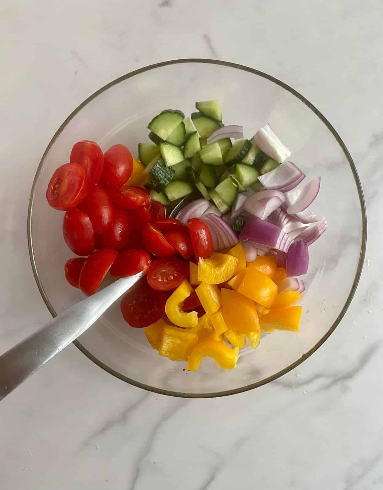 A bowl with chopped cucumbers, tomatoes, red onion and bell pepper for Mediterranean Chopped Salad