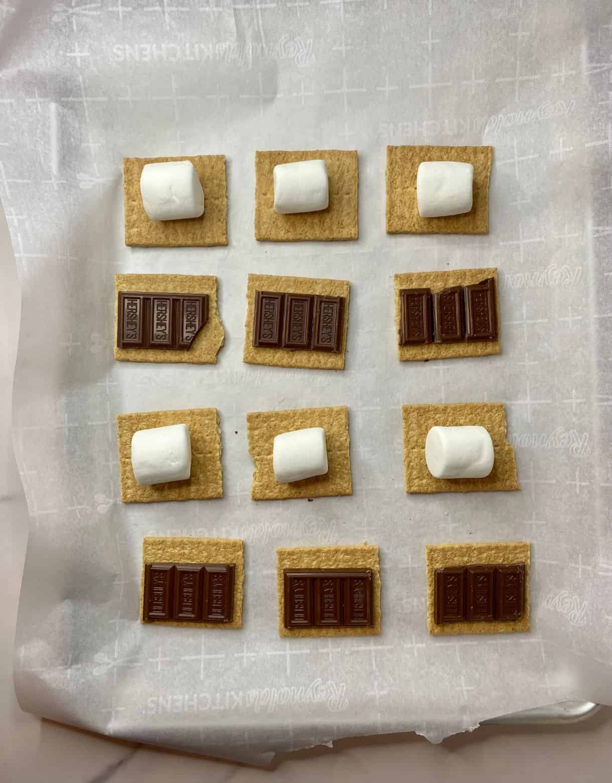 A pan of graham cracker halves, each topped with a piece of chocolate and a marshmallow.