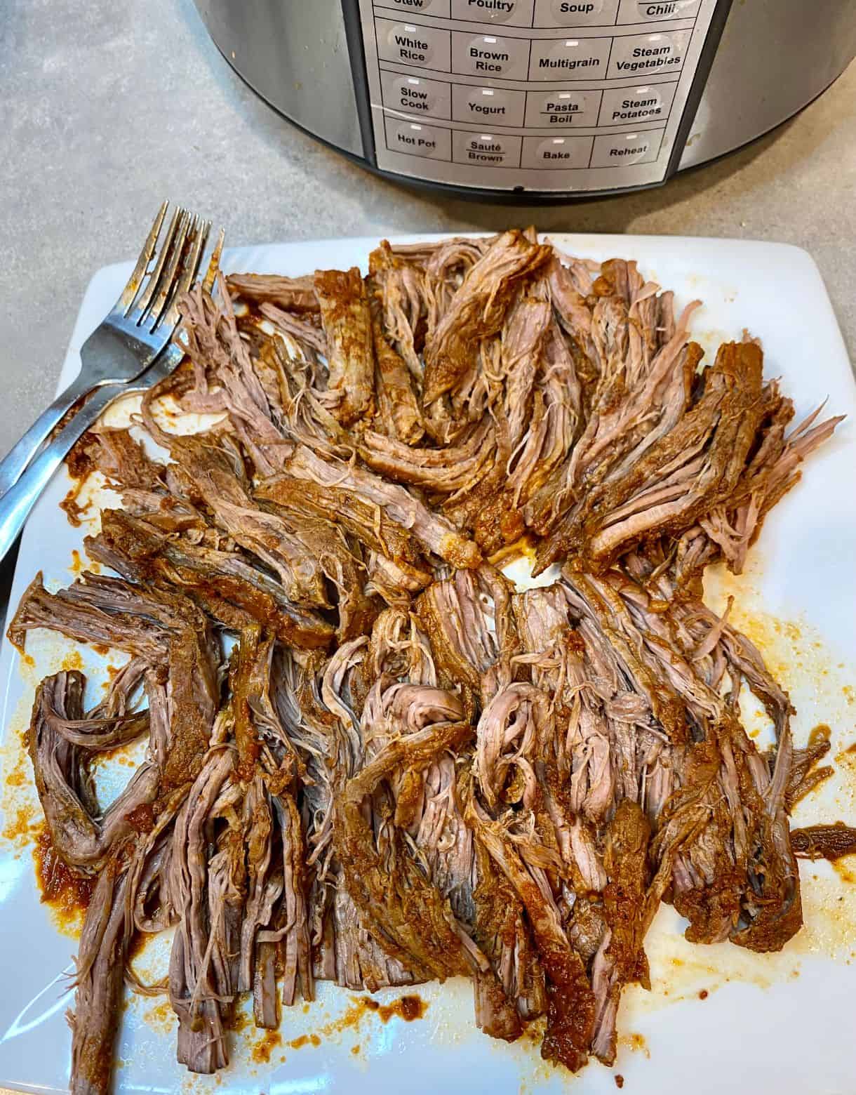 A plate with shredded beef and two forks for Pulled Beef Tacos.