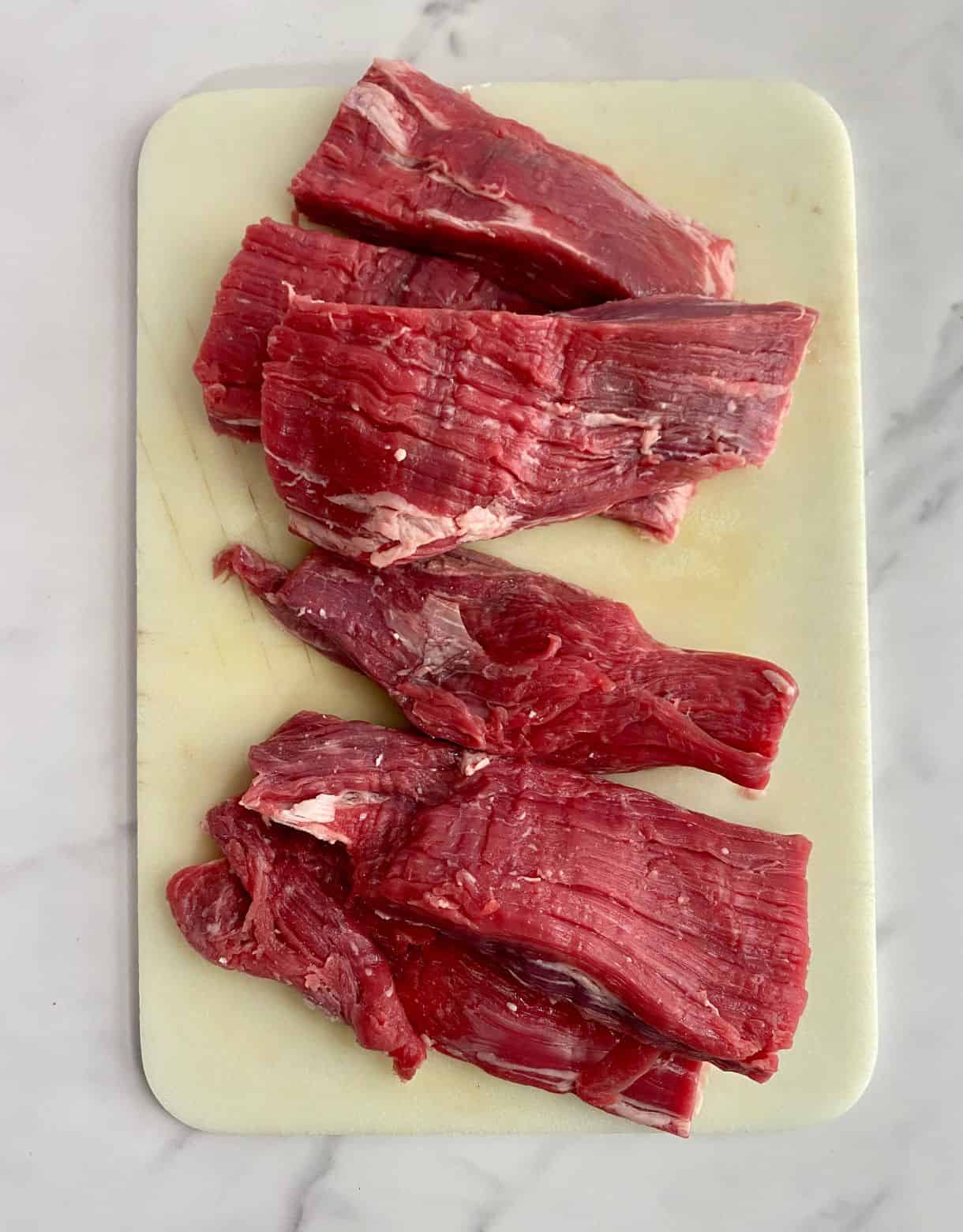 Flank steak on a cutting board cut into 6 large pieces for Pulled Beef Tacos.
