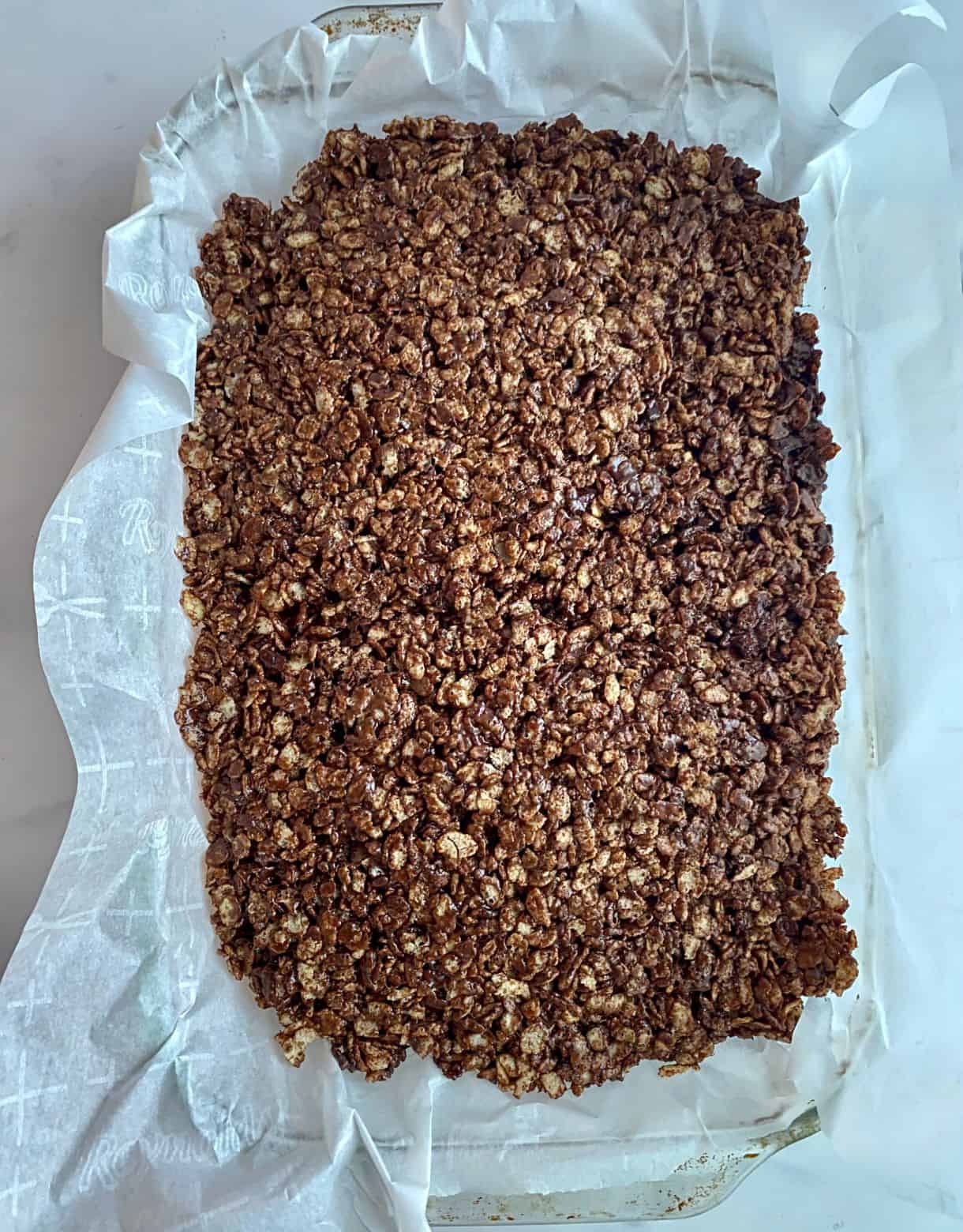 Chocolate Rice Krispie Treats spread into a pan lined with parchment paper.