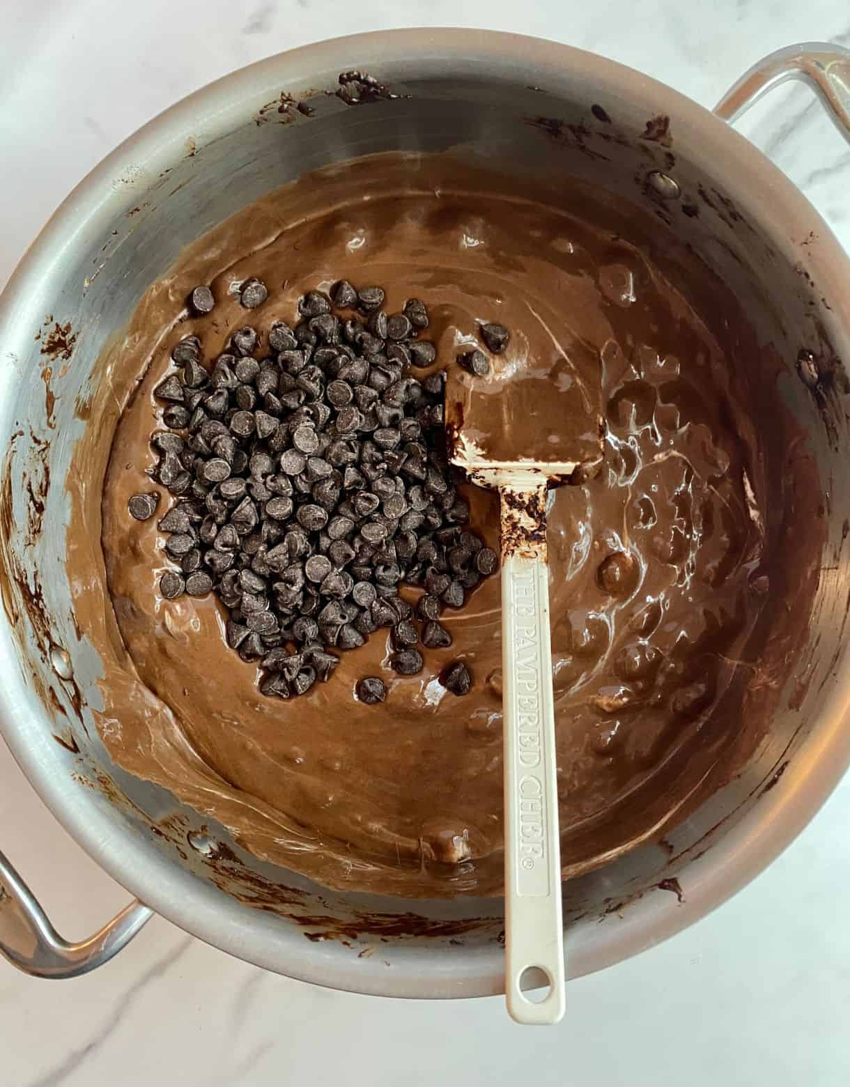 A pot with melted butter, cocoa powder and mini marshmallows with chocolate chips added but not stirred.