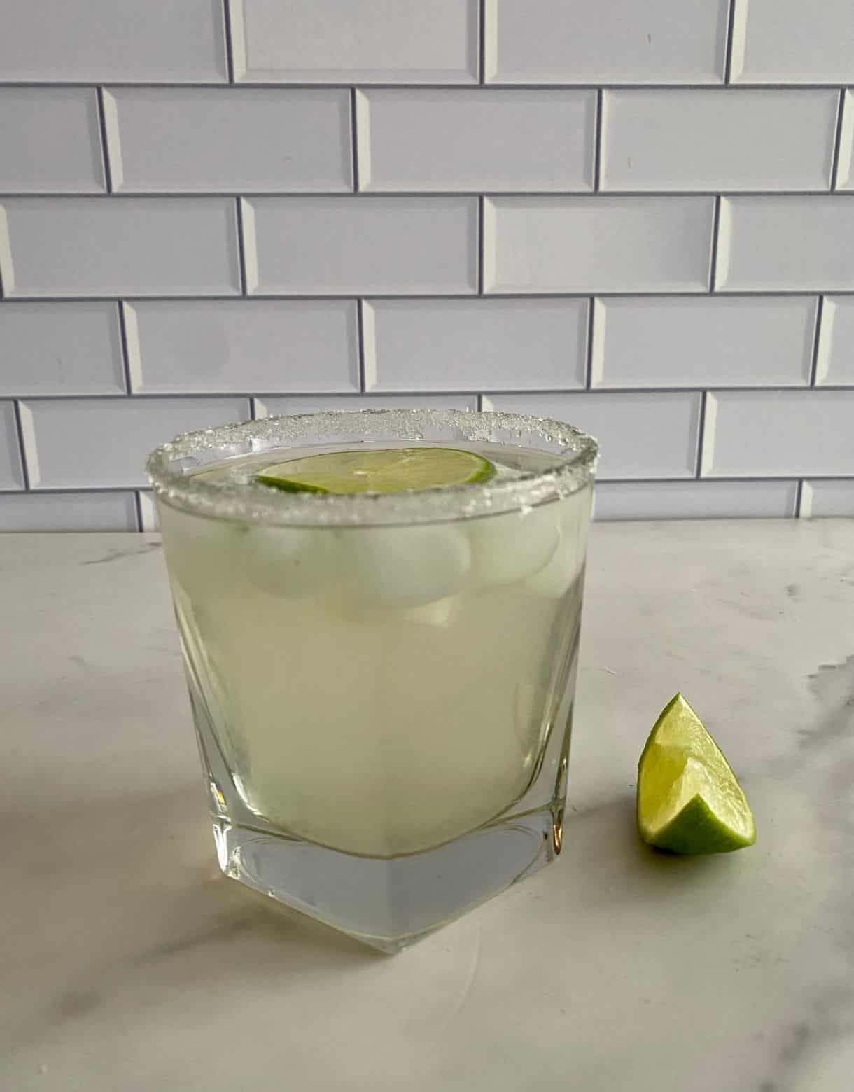 A Coconut Water Cocktail in a glass with a wedge of lime and a salted rim.