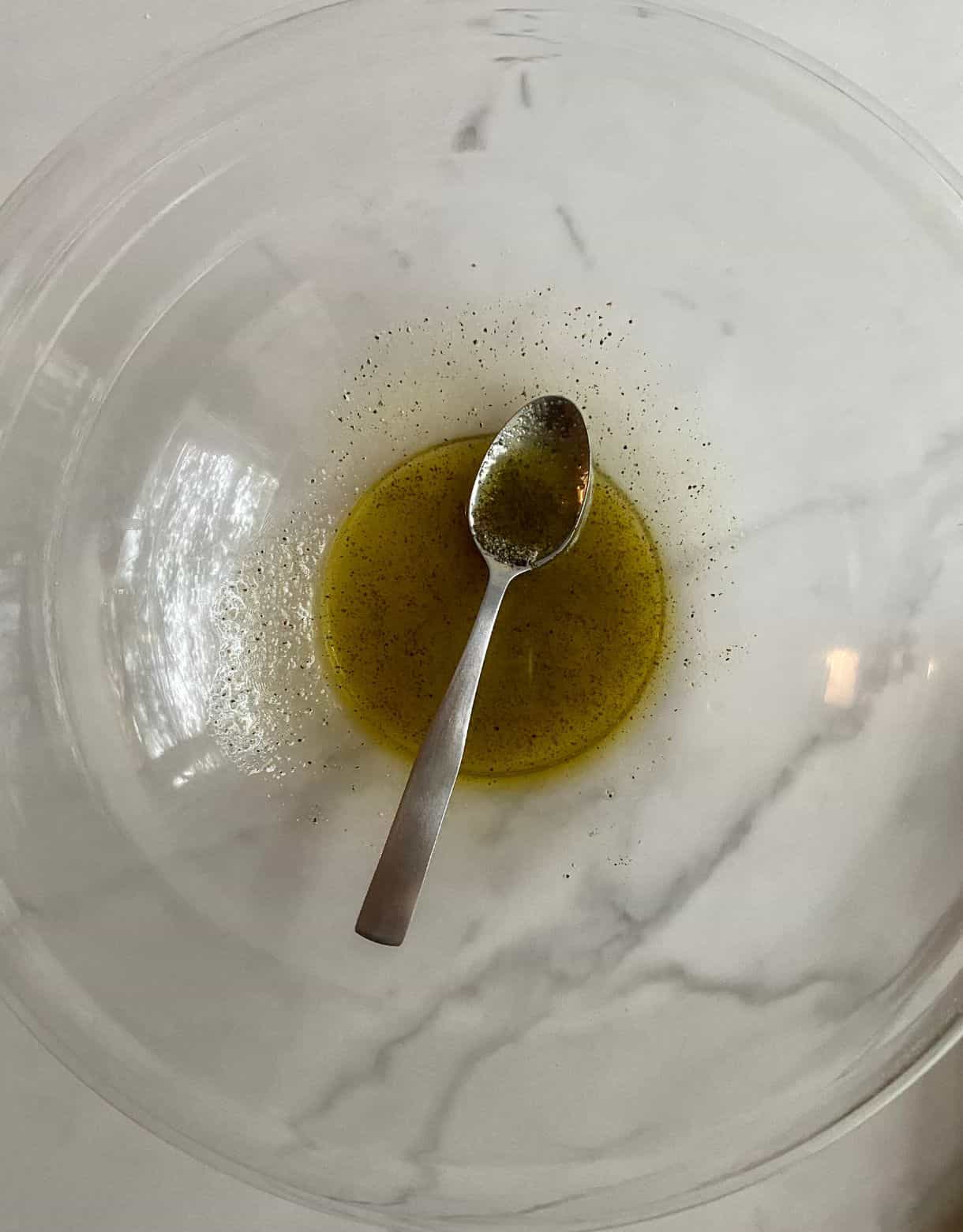 A bowl with a spoon and olive oil, salt and pepper mixed together.