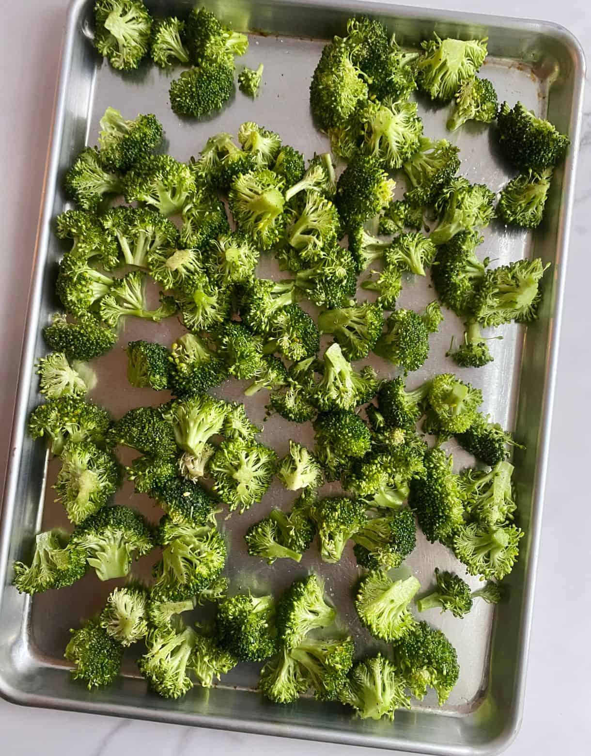 A sheet pan with raw broccoli ready to go in the oven for Sheet Pan Broccoli.