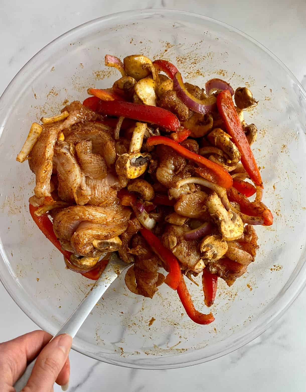 A bowl of raw chicken, bell peppers, onion and mushrooms tossed with olive oil and spices.