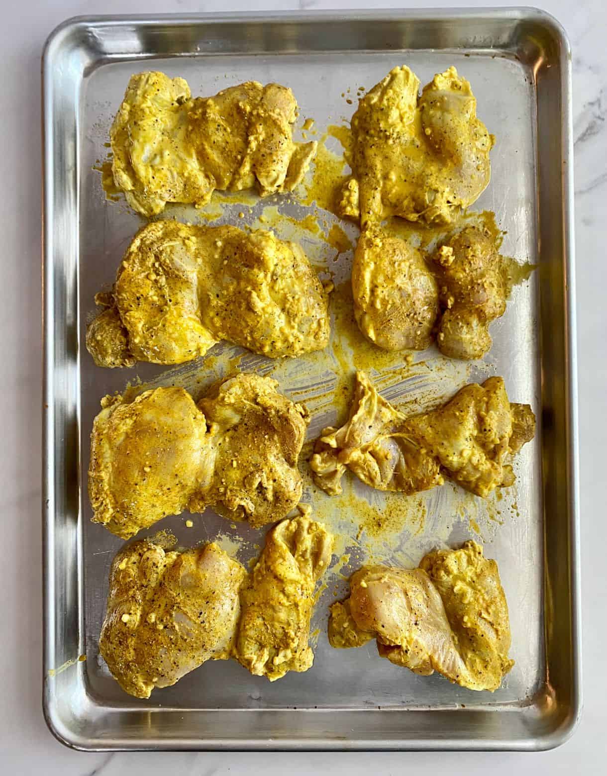A sheet pan with raw marinated chicken thighs.