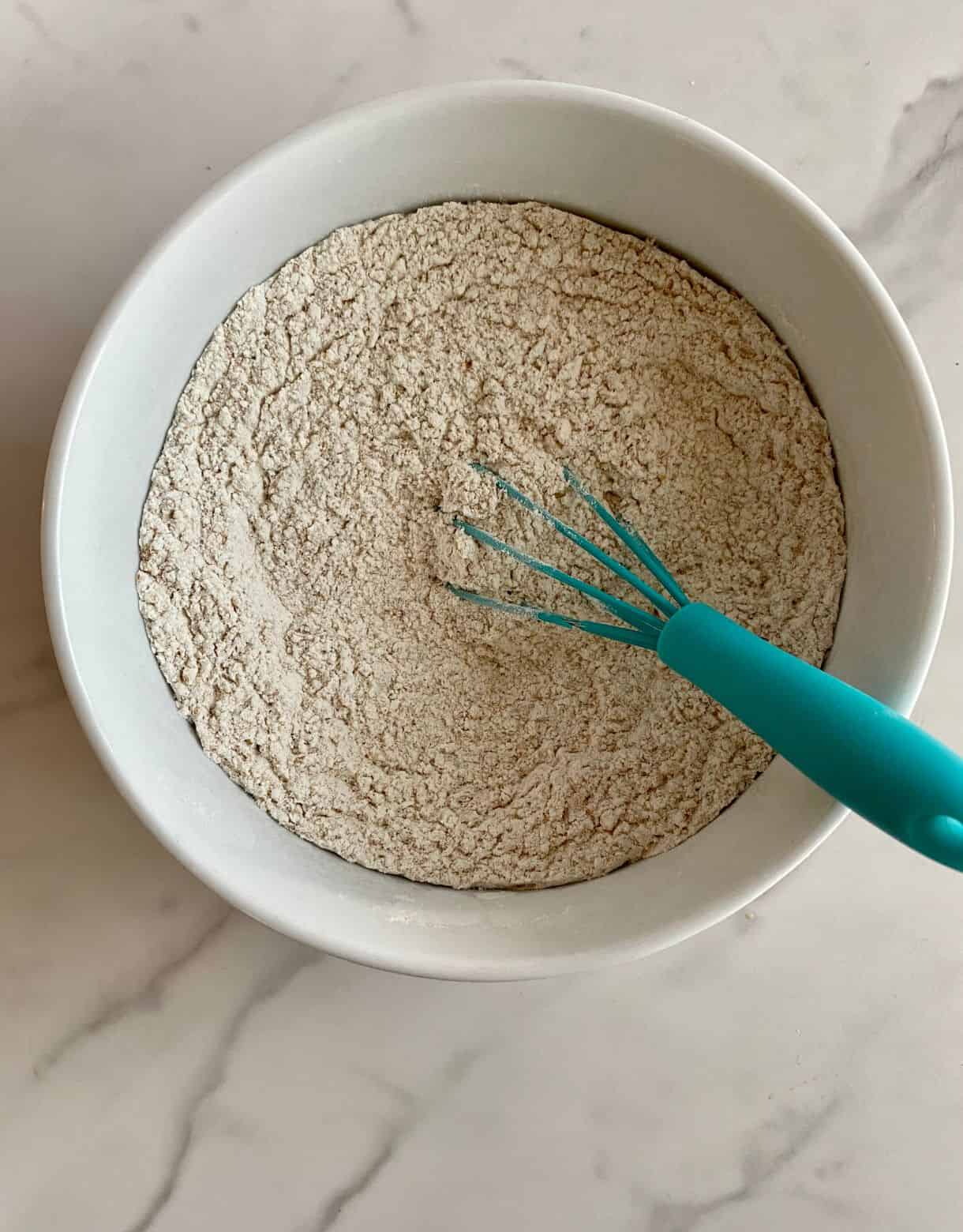 A bowl of all-purpose flour, whole wheat flour and baking soda mixed together with a whisk.