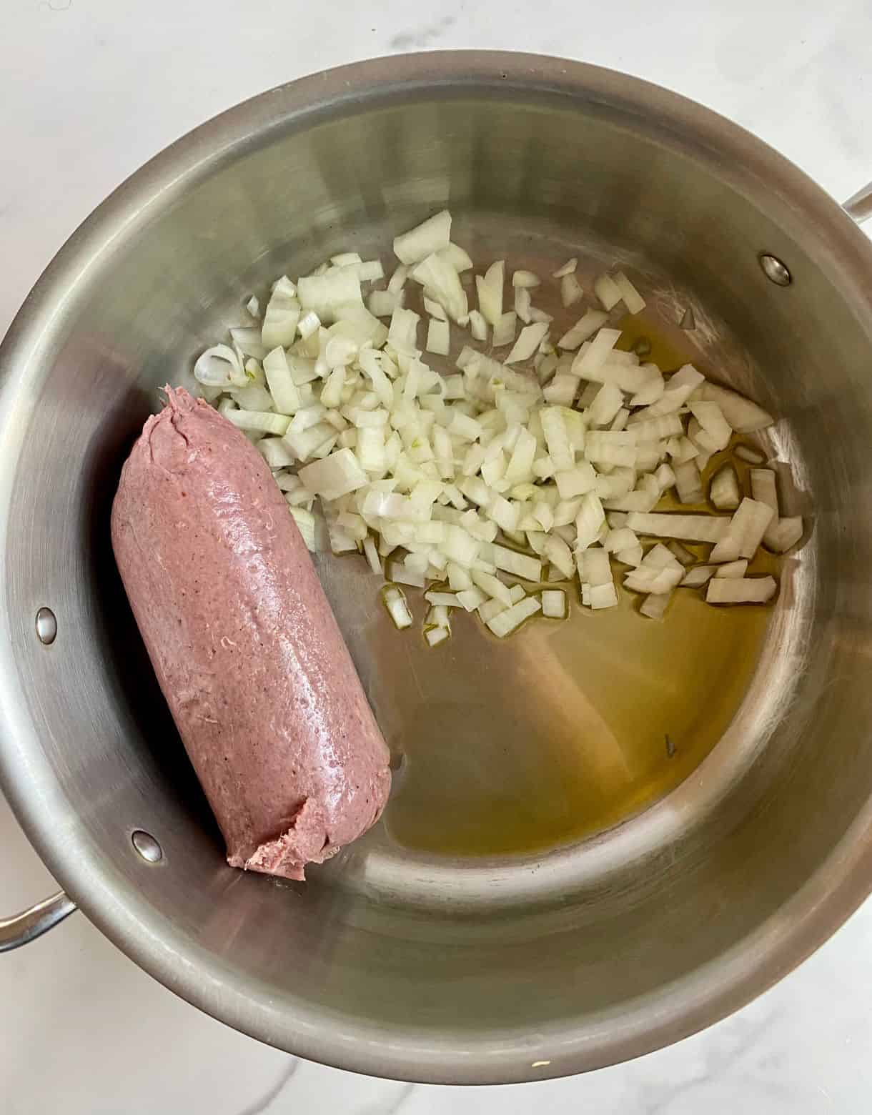 A pot with olive oil, raw diced onion and raw turkey sausage.