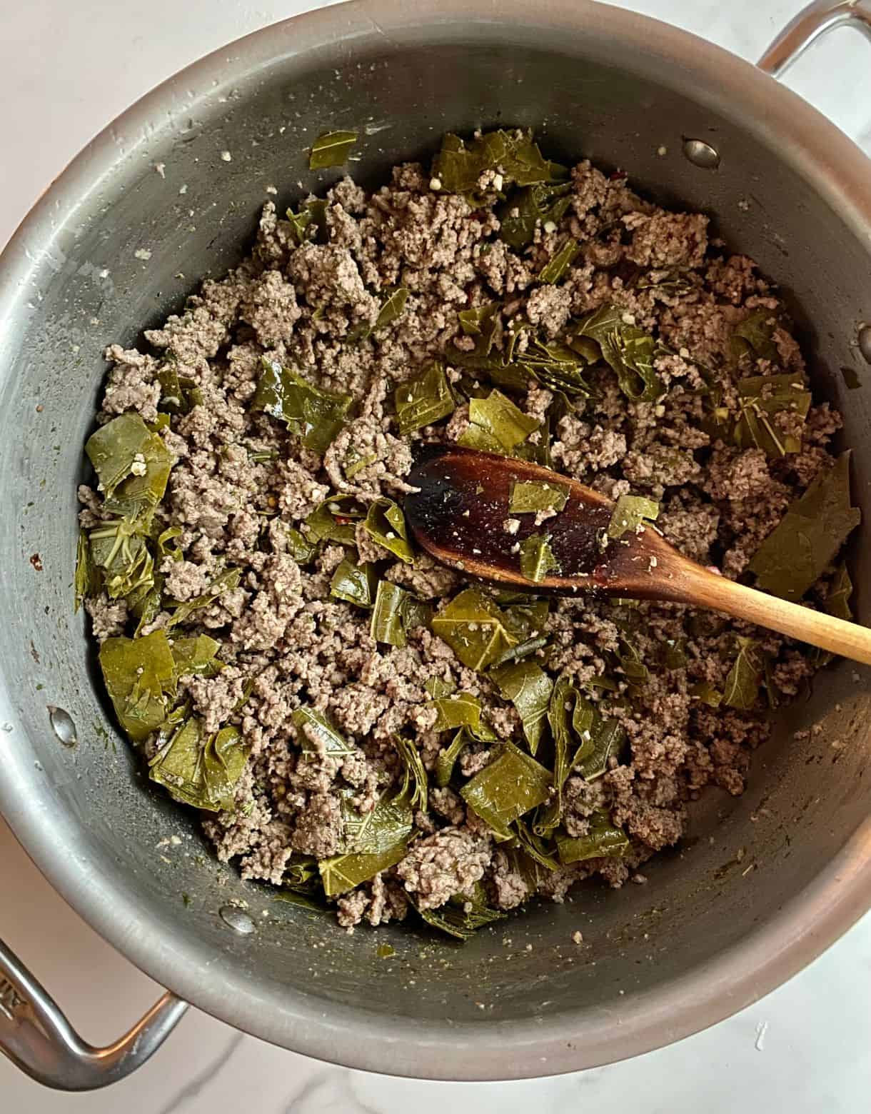 A pot of cooked and crumbled ground beef that is seasoned and has chopped grape leaves added.