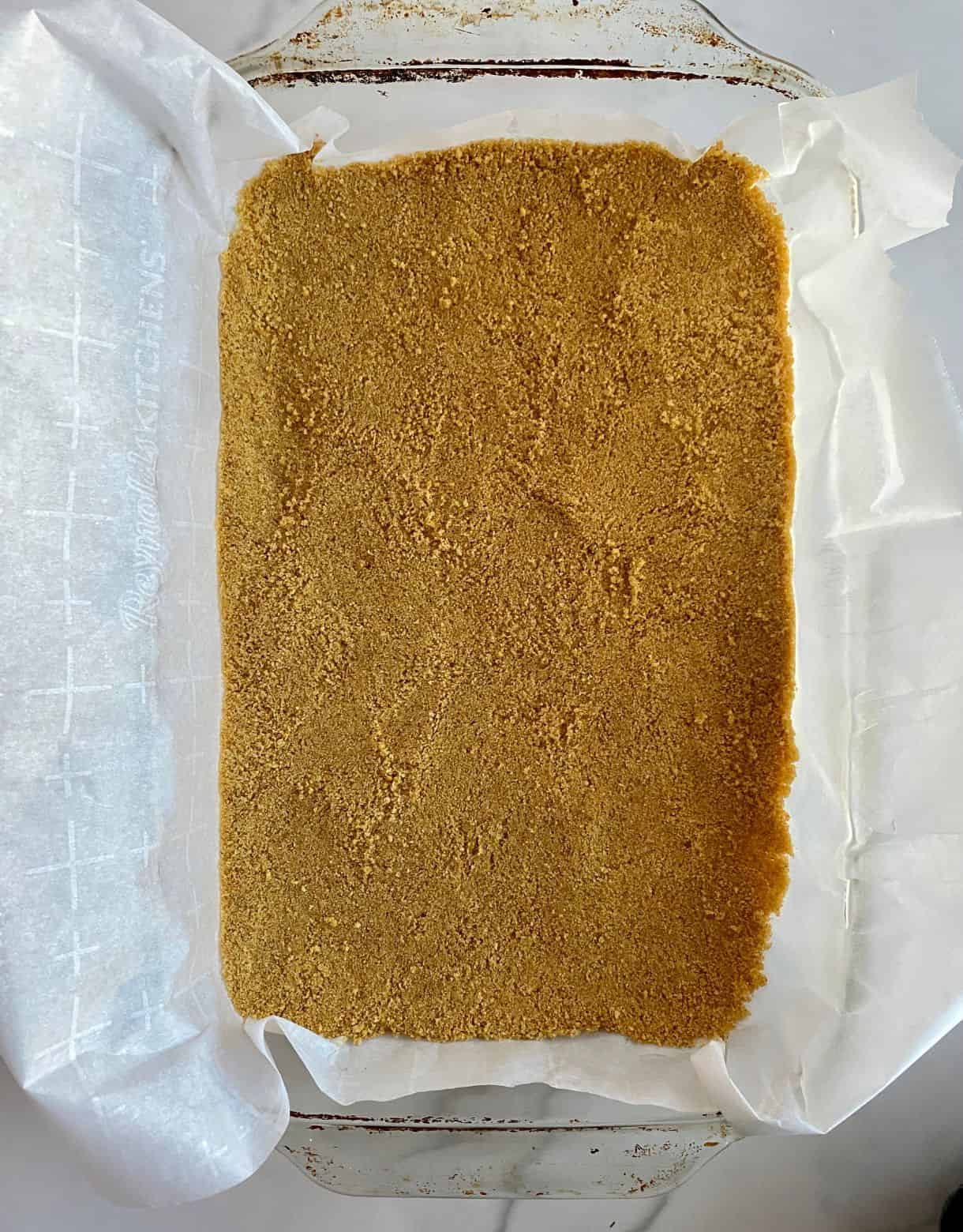 An un-baked graham cracker crust in a 9x13 dish.