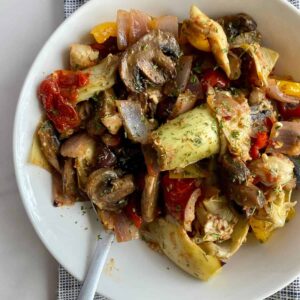 A plate of cooked Mediterranean Roasted Vegetables with mushrooms, tomatoes, onion, bell pepper and artichokes.