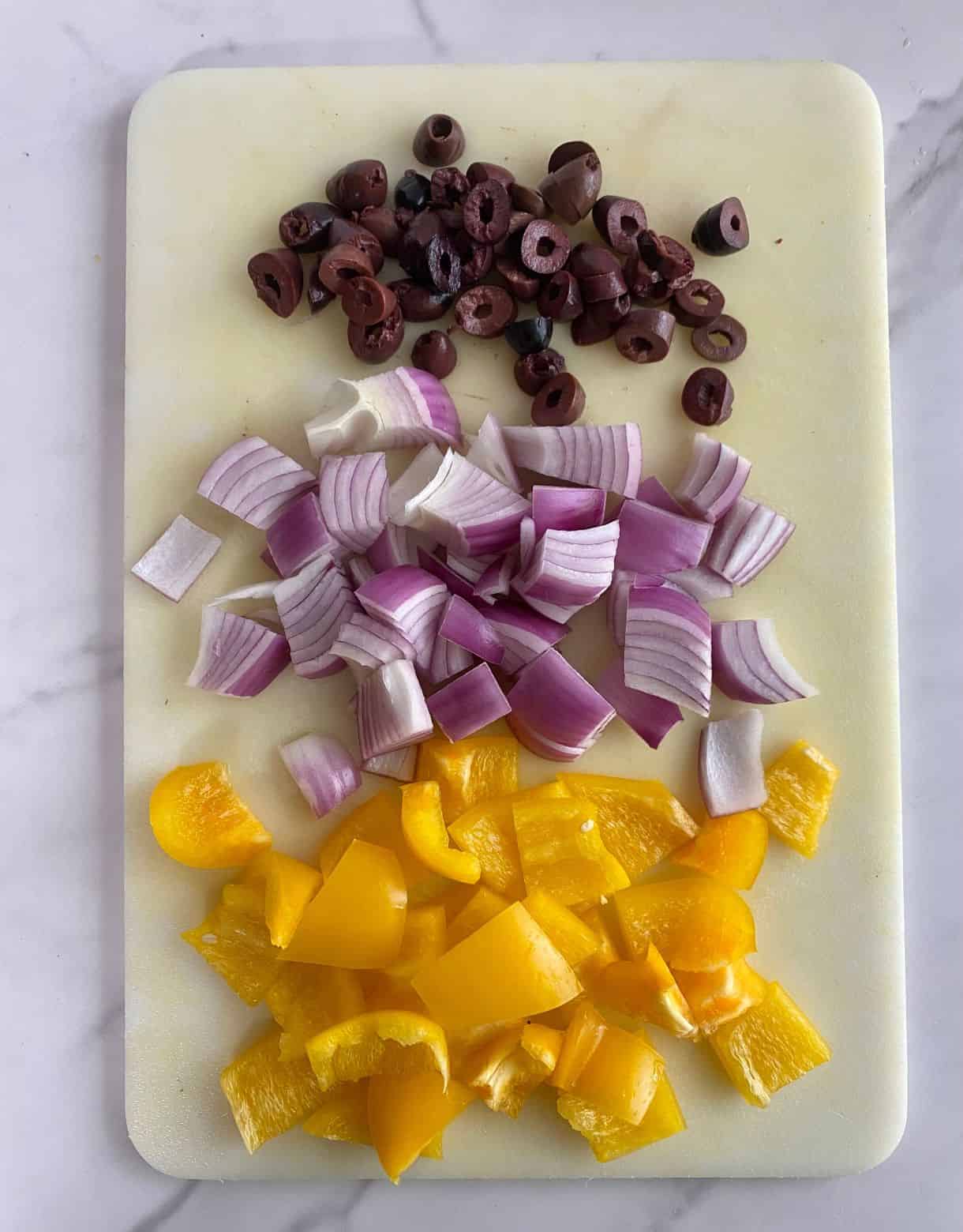 A cutting board with diced onion, bell pepper and sliced olives.