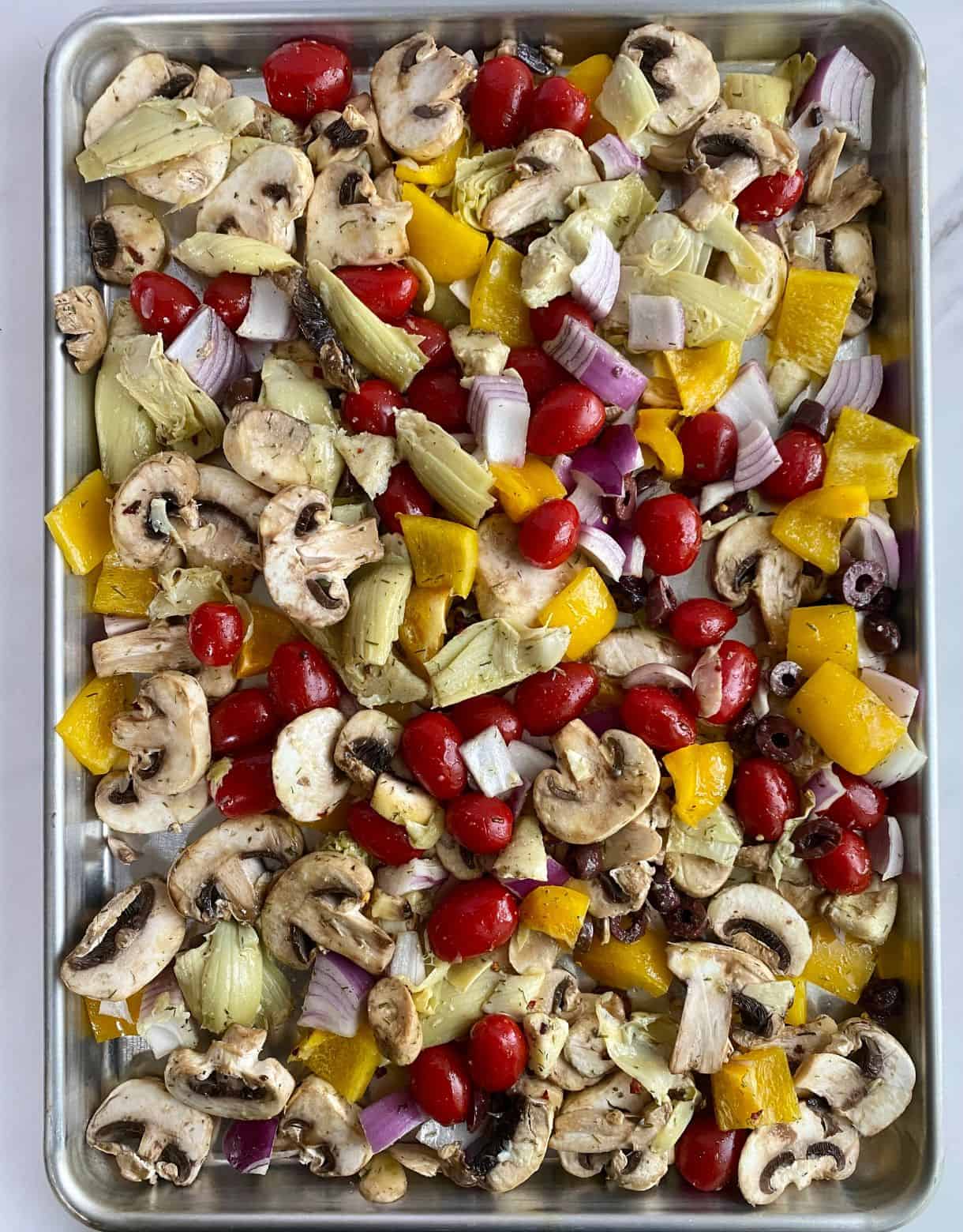 A sheet pan with uncooked Mediterranean Roasted Vegetables.