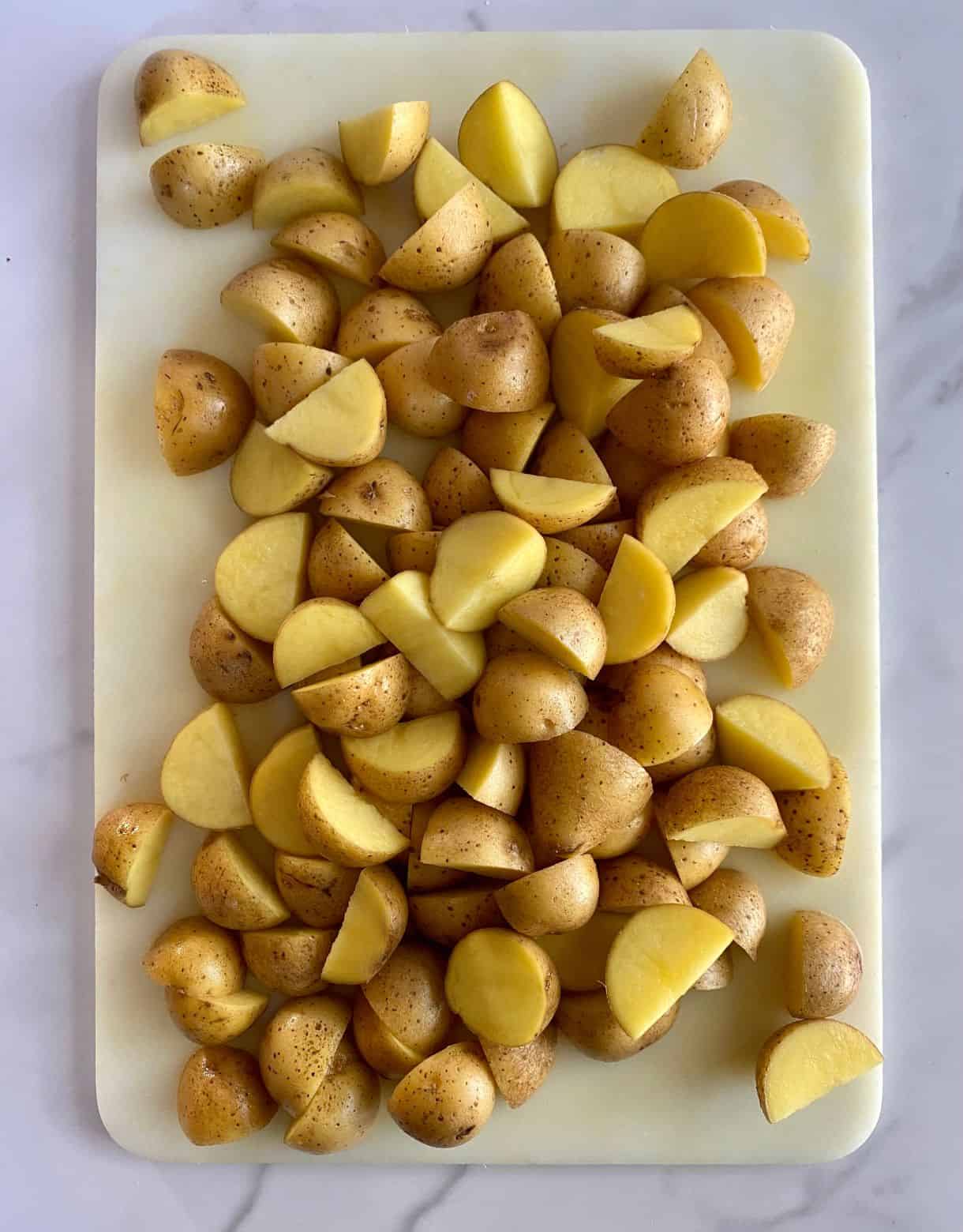 A cutting board with mini potatoes cut into bite-size pieces.
