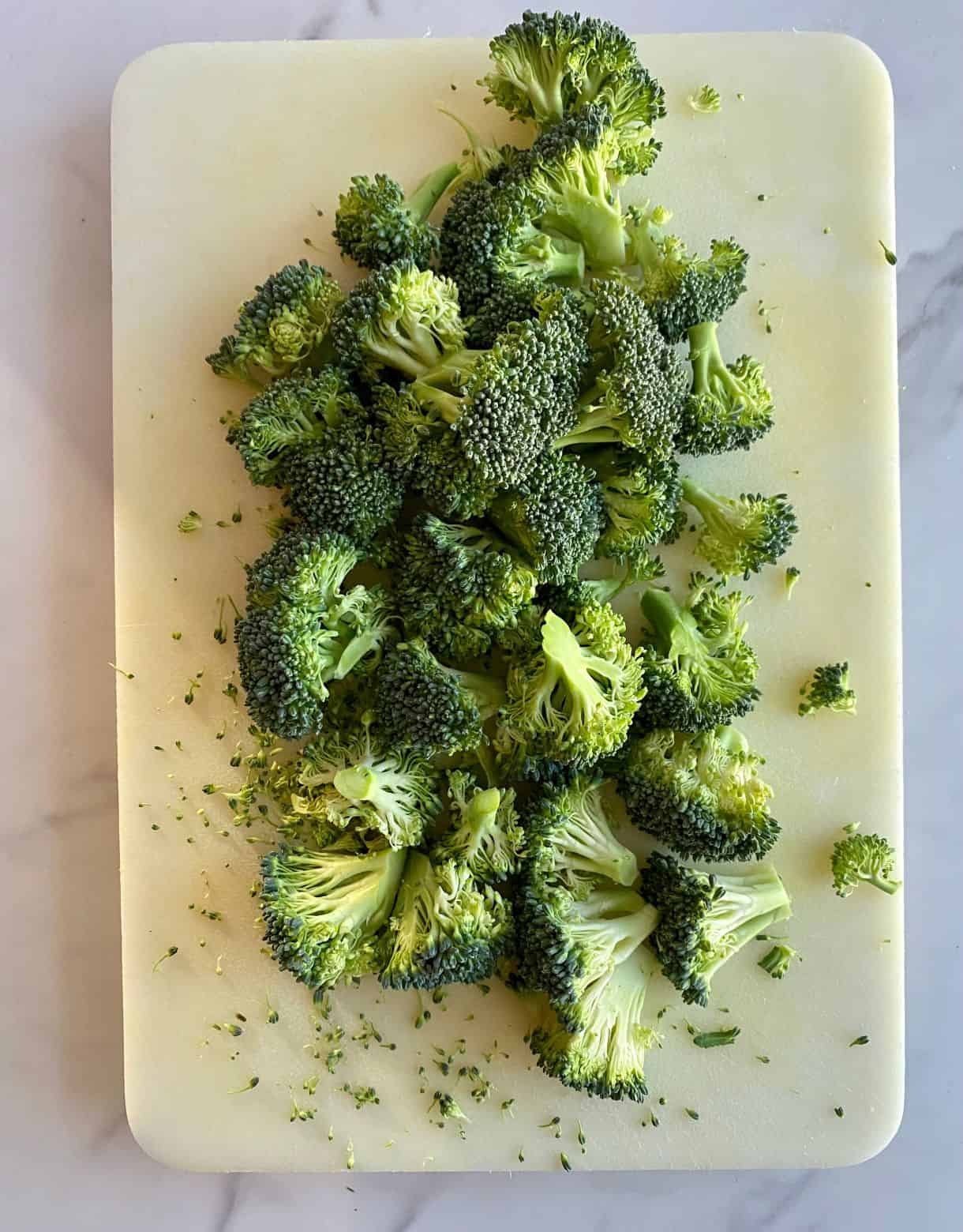 A cutting board with raw broccoli chopped into florets.