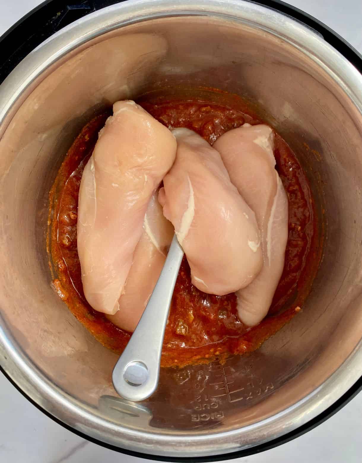 A slow cooker with salsa and raw chicken.