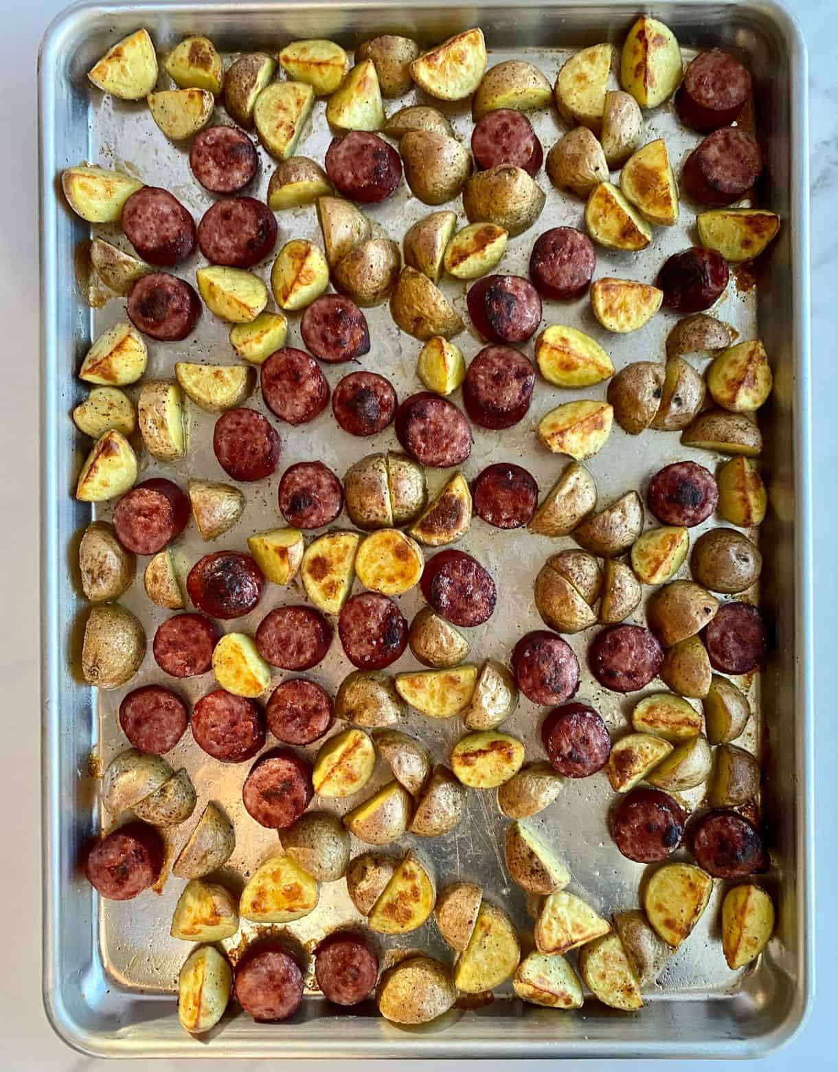 A sheet pan of cooked smoked sausage and potatoes.