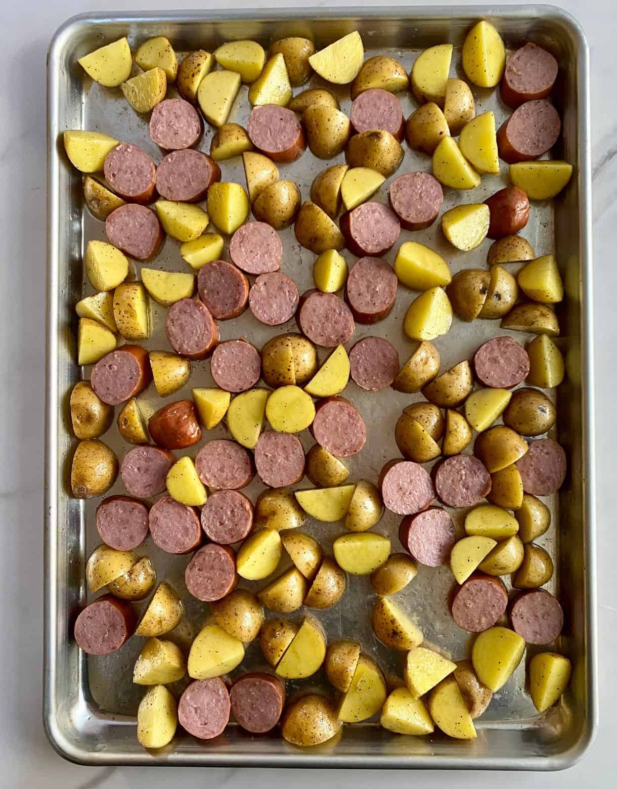 A sheet pan of uncooked sliced smoked turkey sausage and diced potatoes.