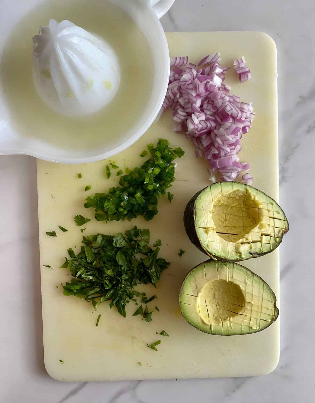 A cutting board with diced red onion, jalapeno, avocado and cilantro plus a juice press with fresh squeezed lime juice.
