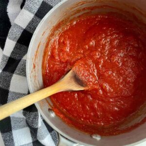 A pot of Spicy Marinara Sauce with a wooden spoon in it.