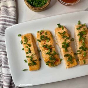 A platter with four pieces of cooked Sweet Chili Salmon topped with green onions.