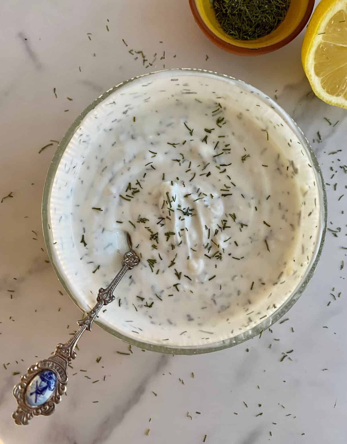 A bowl with Yogurt Dill Sauce and a spoon for serving.