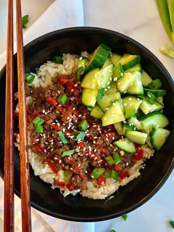 A Bulgogi Bowl with seasoned beef served over cauliflower rice and topped with sliced green onions, sesame seeds, pickled cucumbers and sriracha sauce.