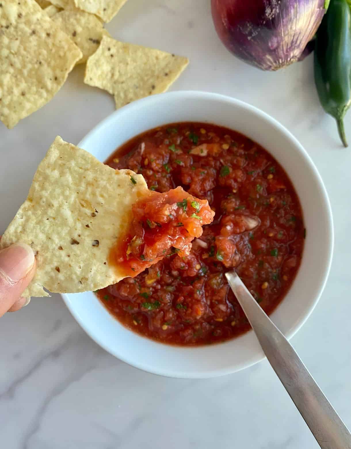 A bowl of Jalapeno Salsa with a spoon and a chip dipped in the salsa.