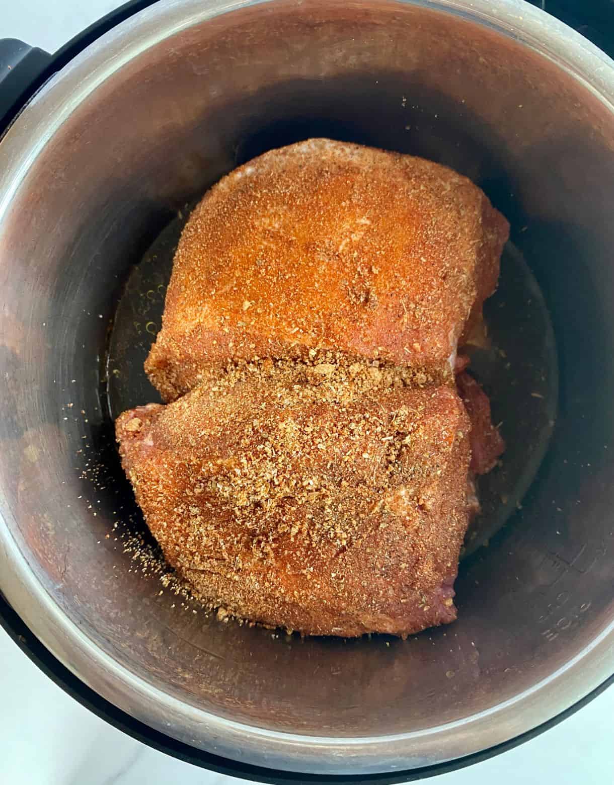 Two pieces of pork loin rubbed with spices and placed in a slow cooker.