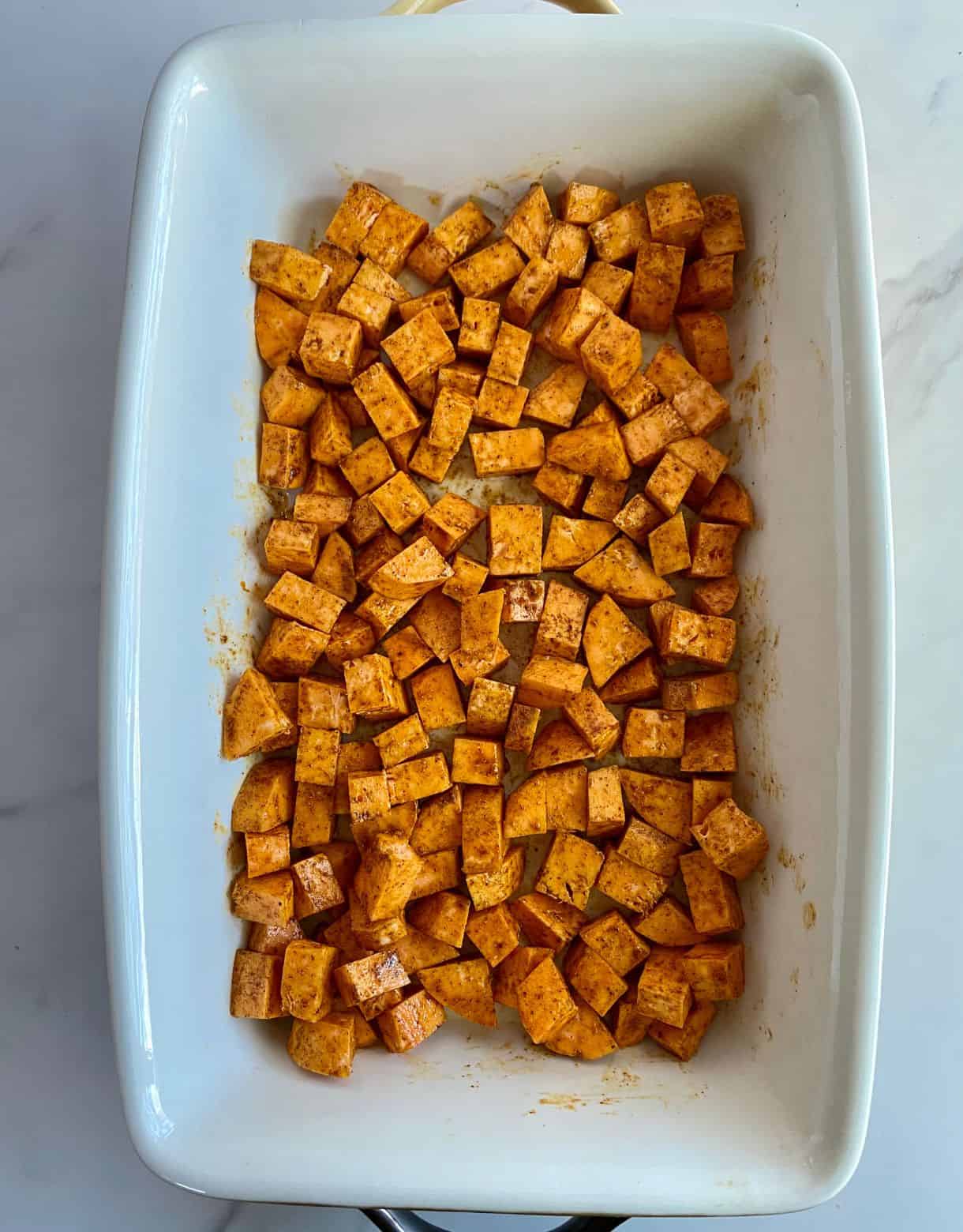 A baking dish with raw seasoned sweet potatoes ready to bake.