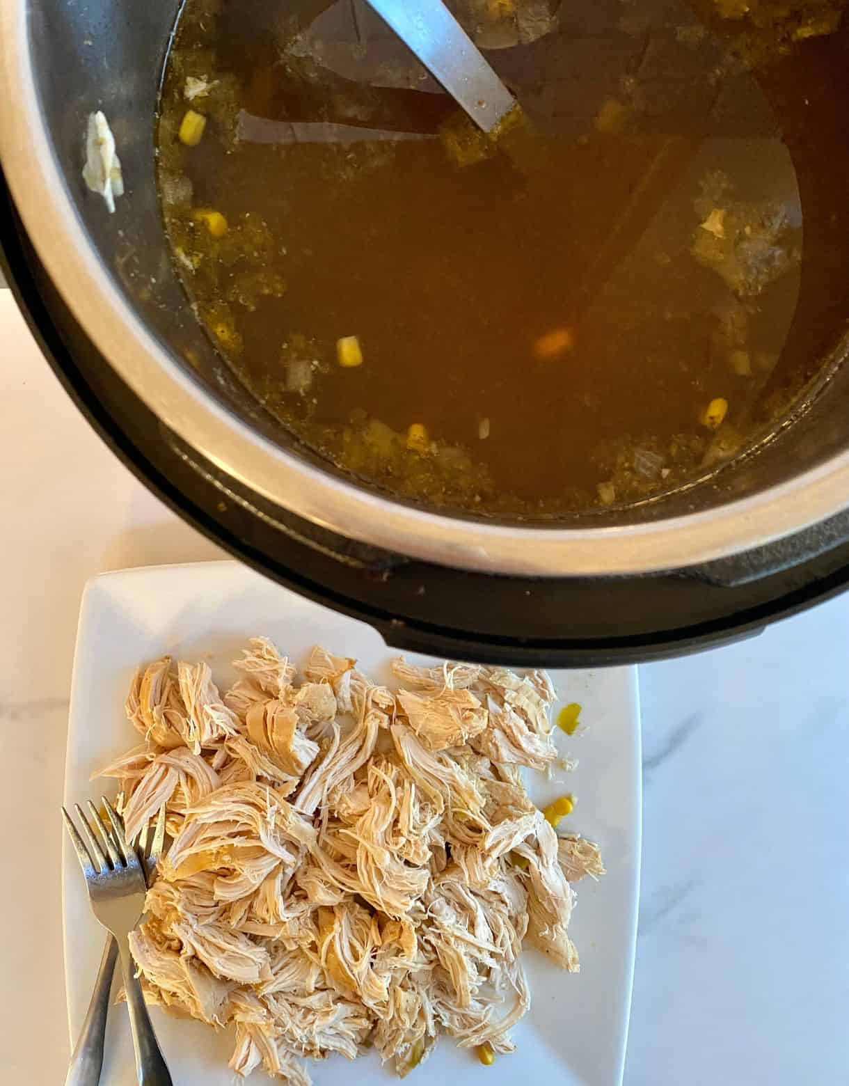 A slow cooker full of Green Chile Chicken Soup and a plate with shredded chicken ready to add to the soup.