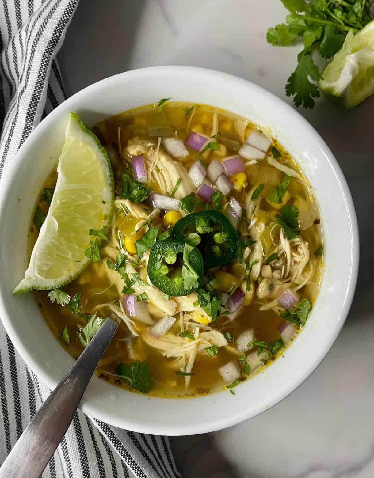 A bowl of Green Chile Chicken Soup with a spoon and a wedge of lime.