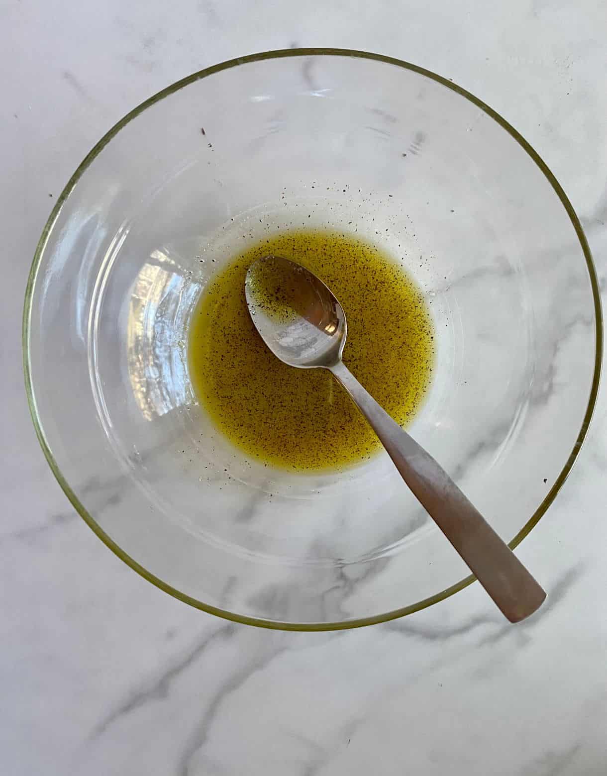 A bowl with a spoon and olive oil, salt and pepper stirred together.