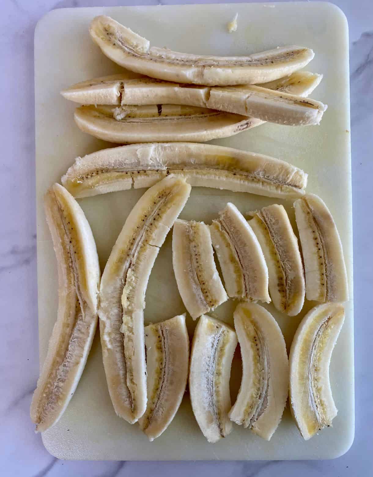 A cutting board with peeled bananas sliced in half lengthwise.