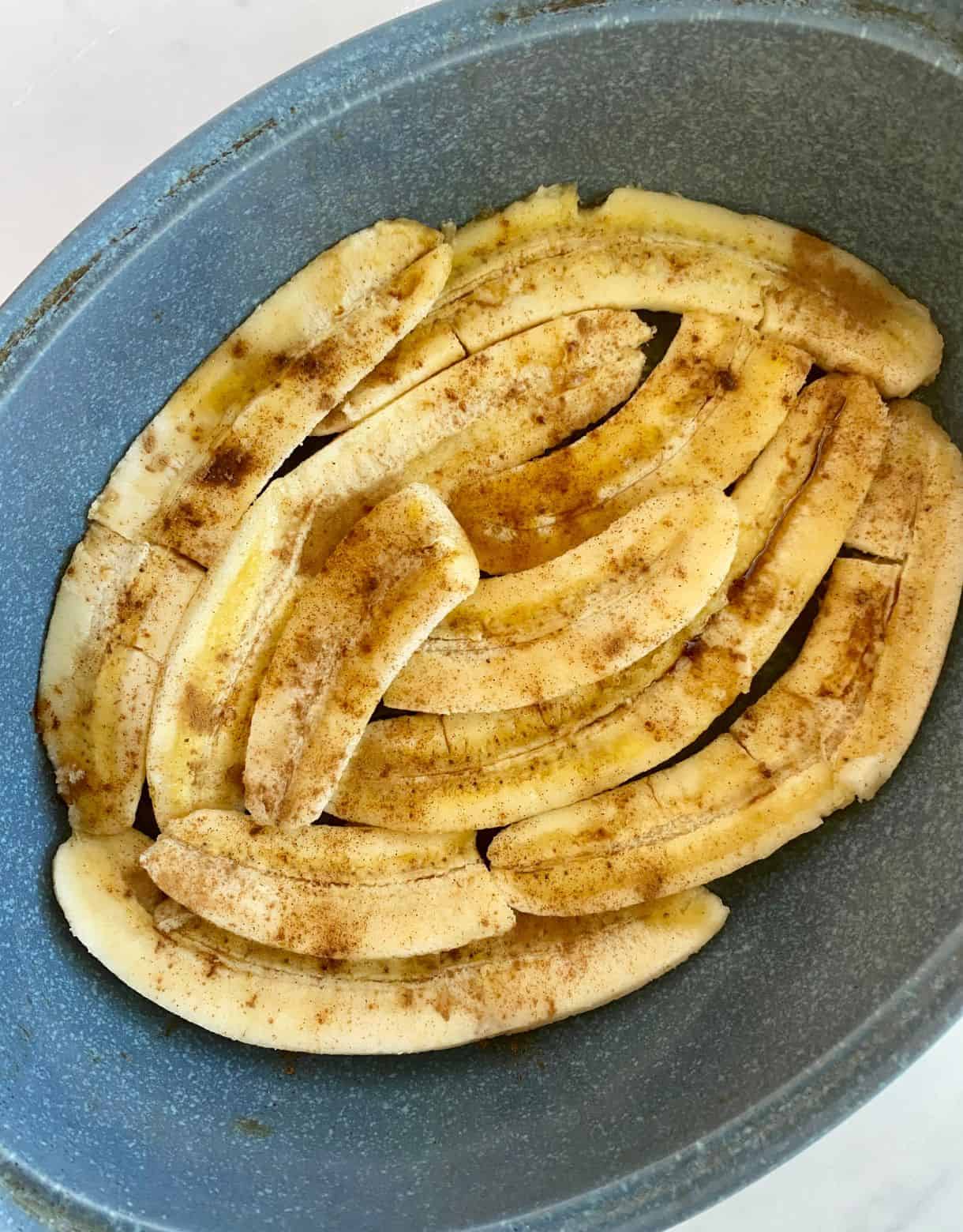 A dish with bananas sliced in half lengthwise then sprinkled with bourbon, vanilla and cinnamon and ready to go in the oven for Healthy Bananas Foster.