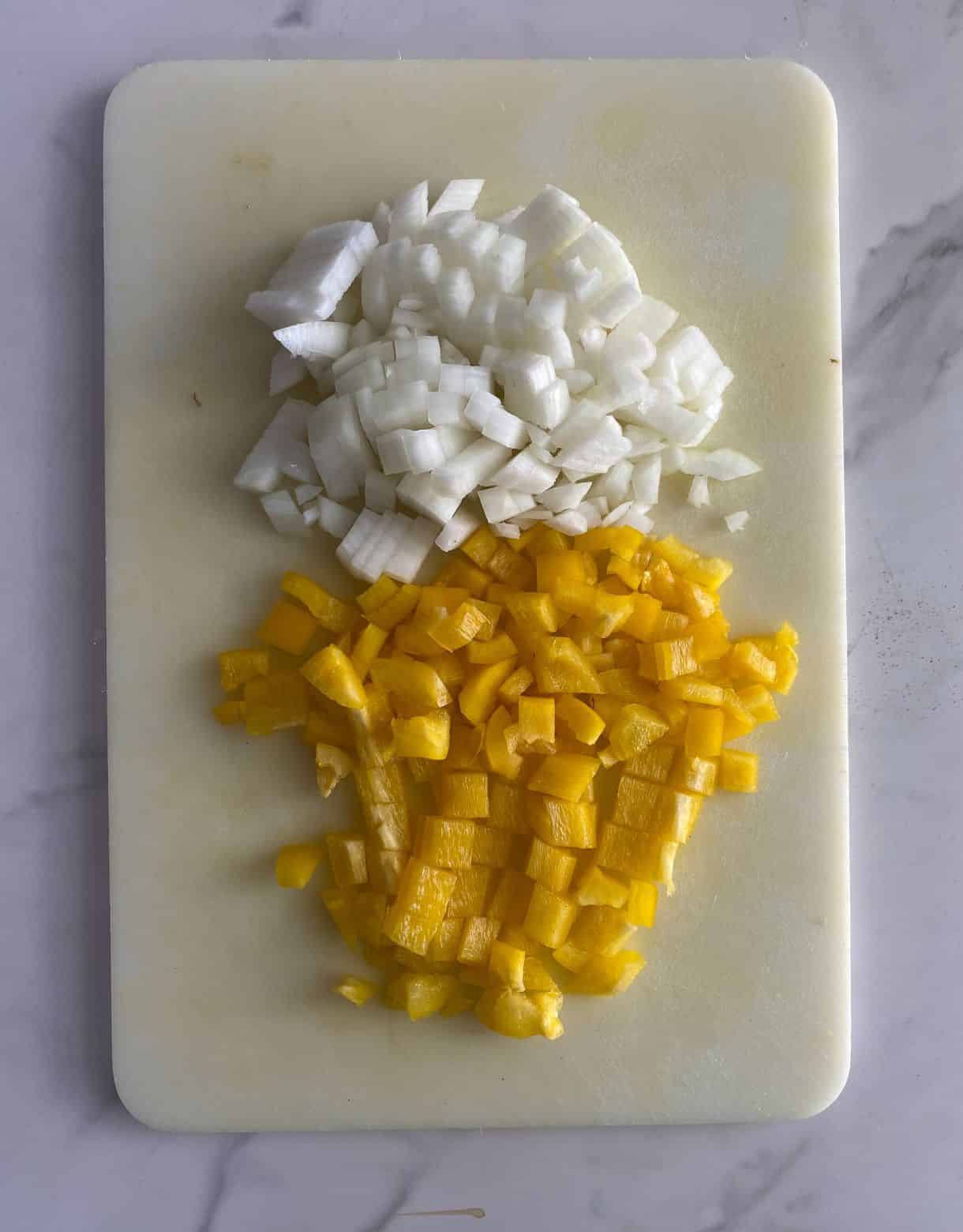 A cutting board with diced onion and bell pepper.