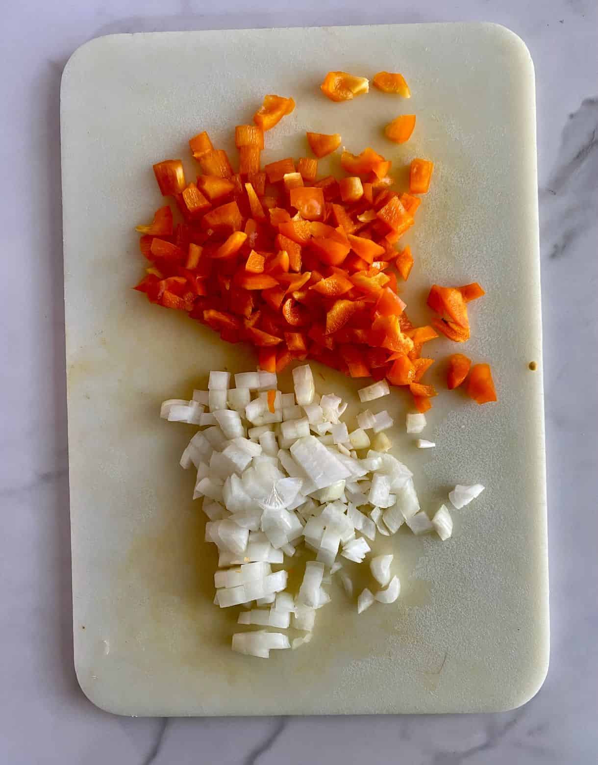 A cutting board with diced onion and bell pepper.