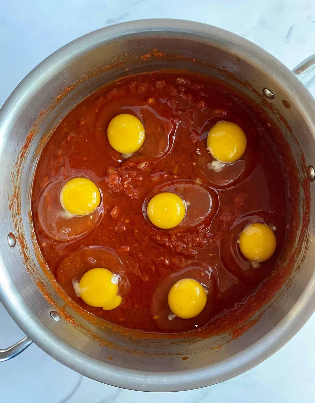A pot with tomato sauce with raw eggs gently nestled on top.