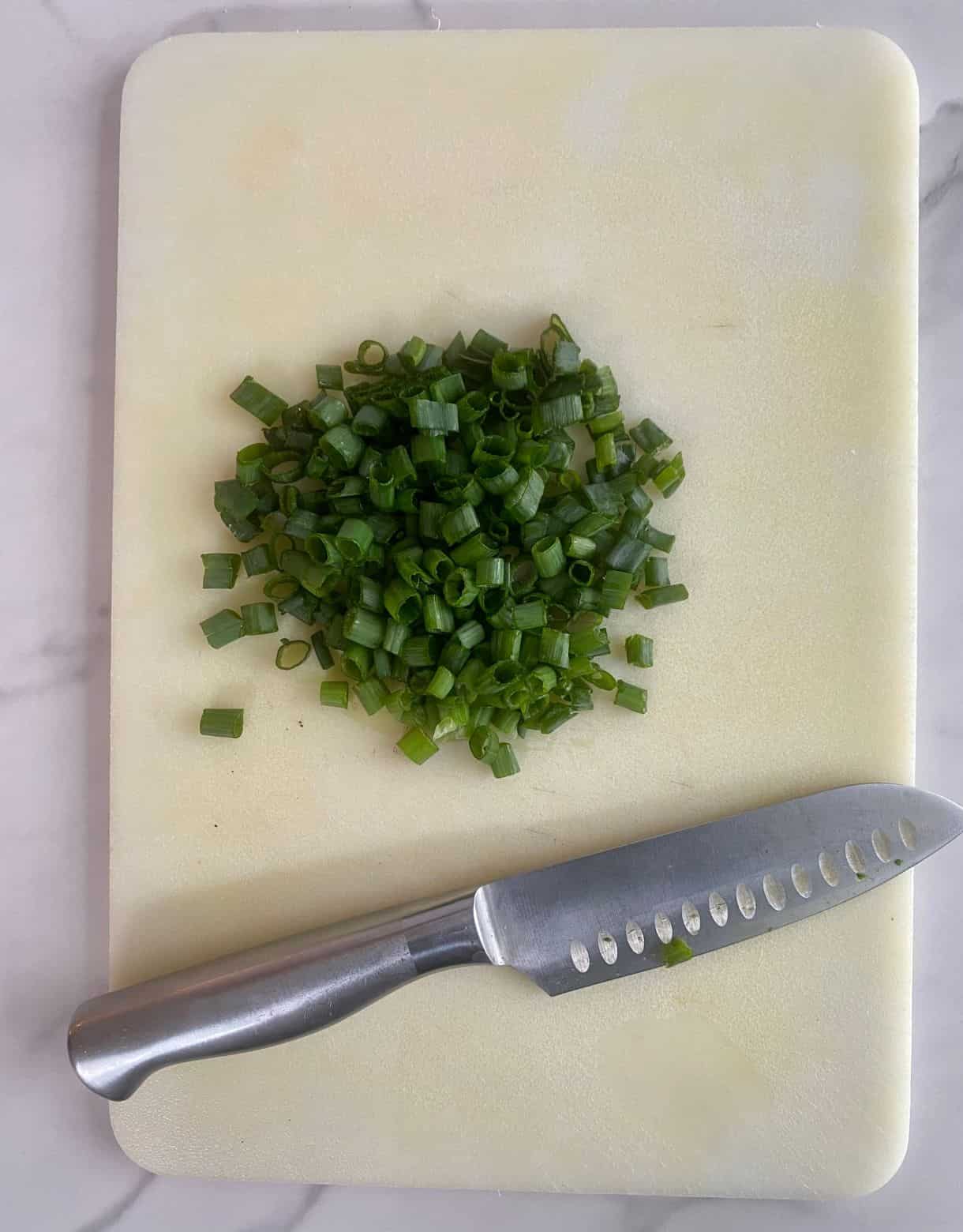 A cutting board with a knife and sliced scallions.